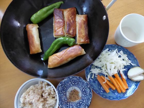 テーブルに並ぶフライパンにのった春巻きや、茶碗に盛った玄米など